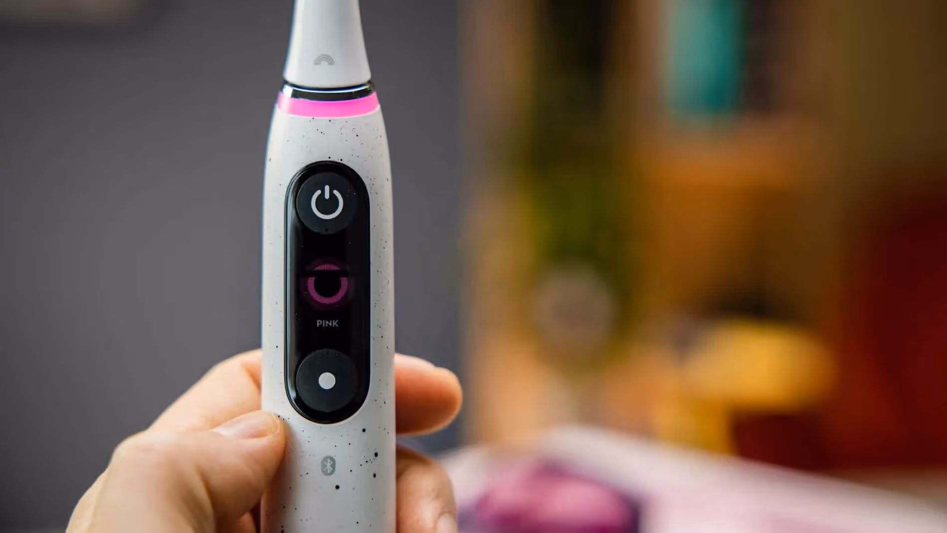 Szczoteczka Oral-B iO trzymana w dłoni, z widocznym przyciskiem i wyświetlaczem.