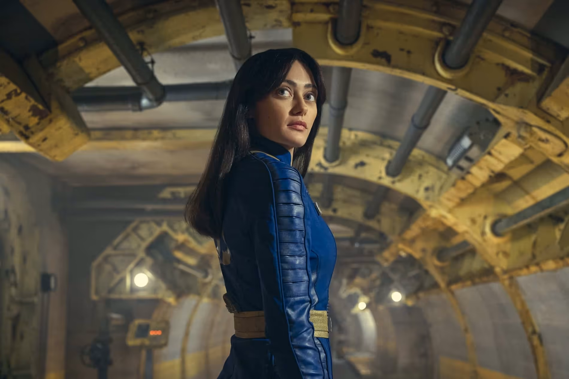Lucy w niebieskim kombinezonie w kadrze z serialu „Fallout”.